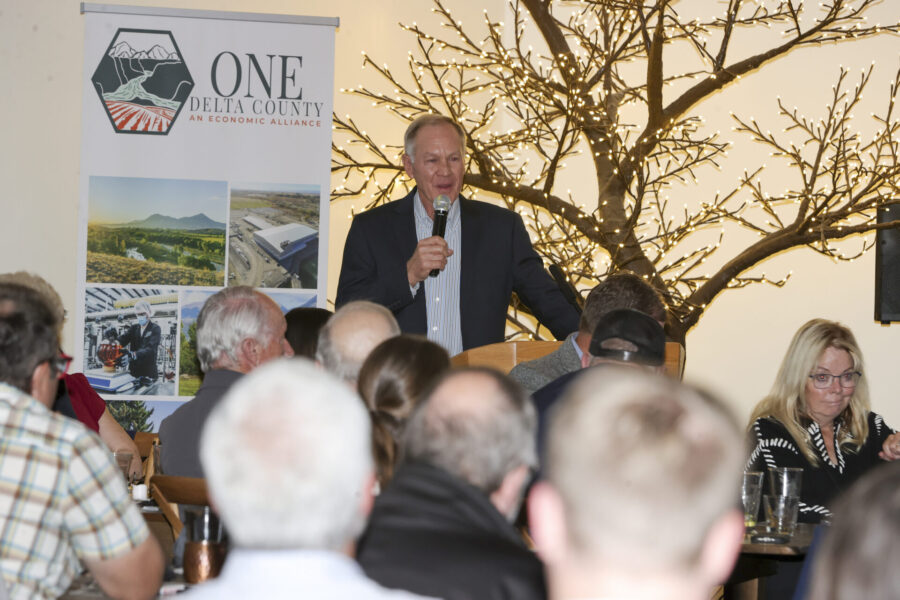 Greg Pope, speaks tot eh audience next to One Delta Countys banner and a tree filled with twinkle lights.